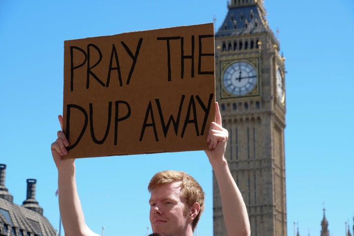 Protesters hold placards as they attend a demonstration against the Conservative party alliance with the DUP in Parliament Sq