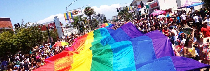 A large rainbow flag waves over a crowd.