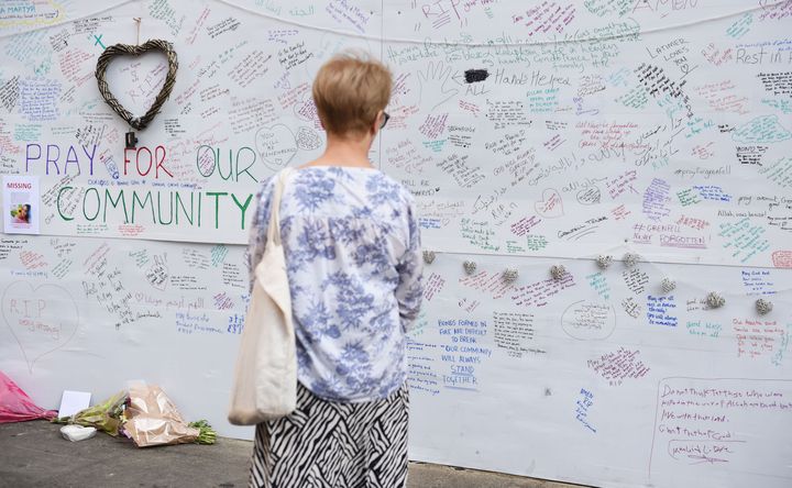 A woman reads a wall of tributes close to Grenfell Tower