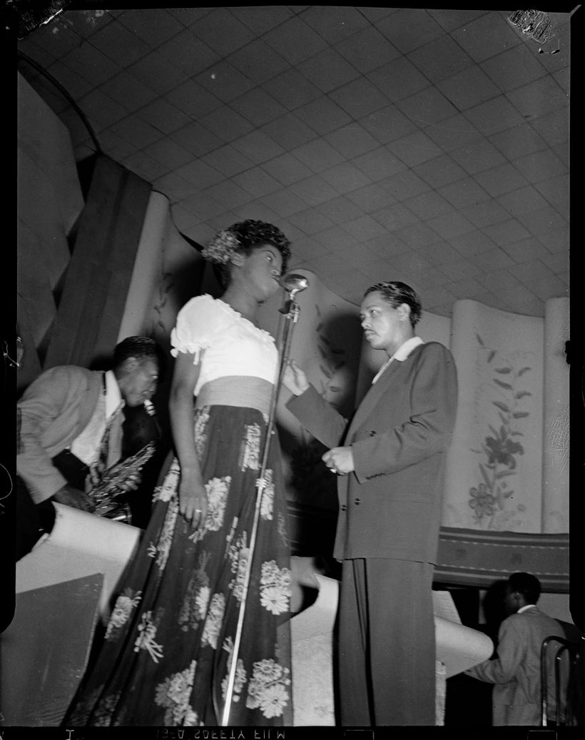 Billy Eckstine conducting his orchestra with Sarah Vaughan in flowered skirt at microphone, and Charlie Parker on saxophone i