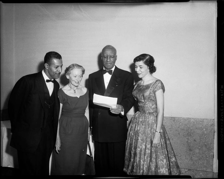 Rev. Charles Foggie, Florence Reizenstein, A. Philip Randolph holding document, and Marion Bond Jordan, standing in interior with marble wainscoting, c. 1950-1965. (in Holocaust Center Teenie Harris Exhibit)