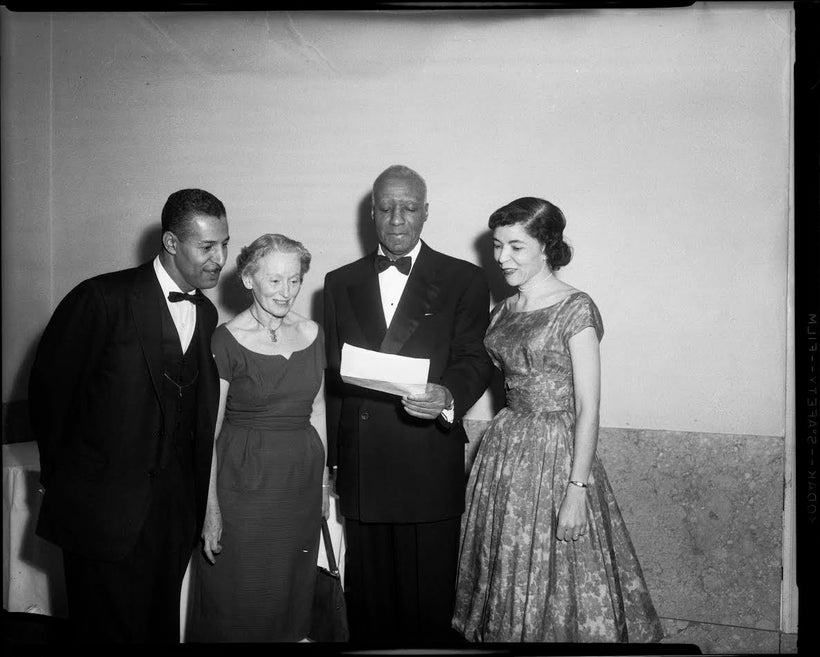 Rev. Charles Foggie, Florence Reizenstein, A. Philip Randolph holding document, and Marion Bond Jordan, standing in interior