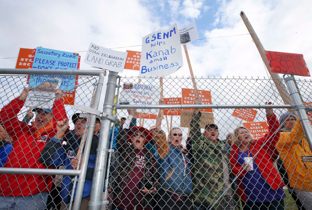 Protesters hold signs and chant behind a security fence as U.S. Secretary of the Interior Ryan Zinke arrives at Kanab Airport for departure on May 10, 2017, in Kanab, Utah.