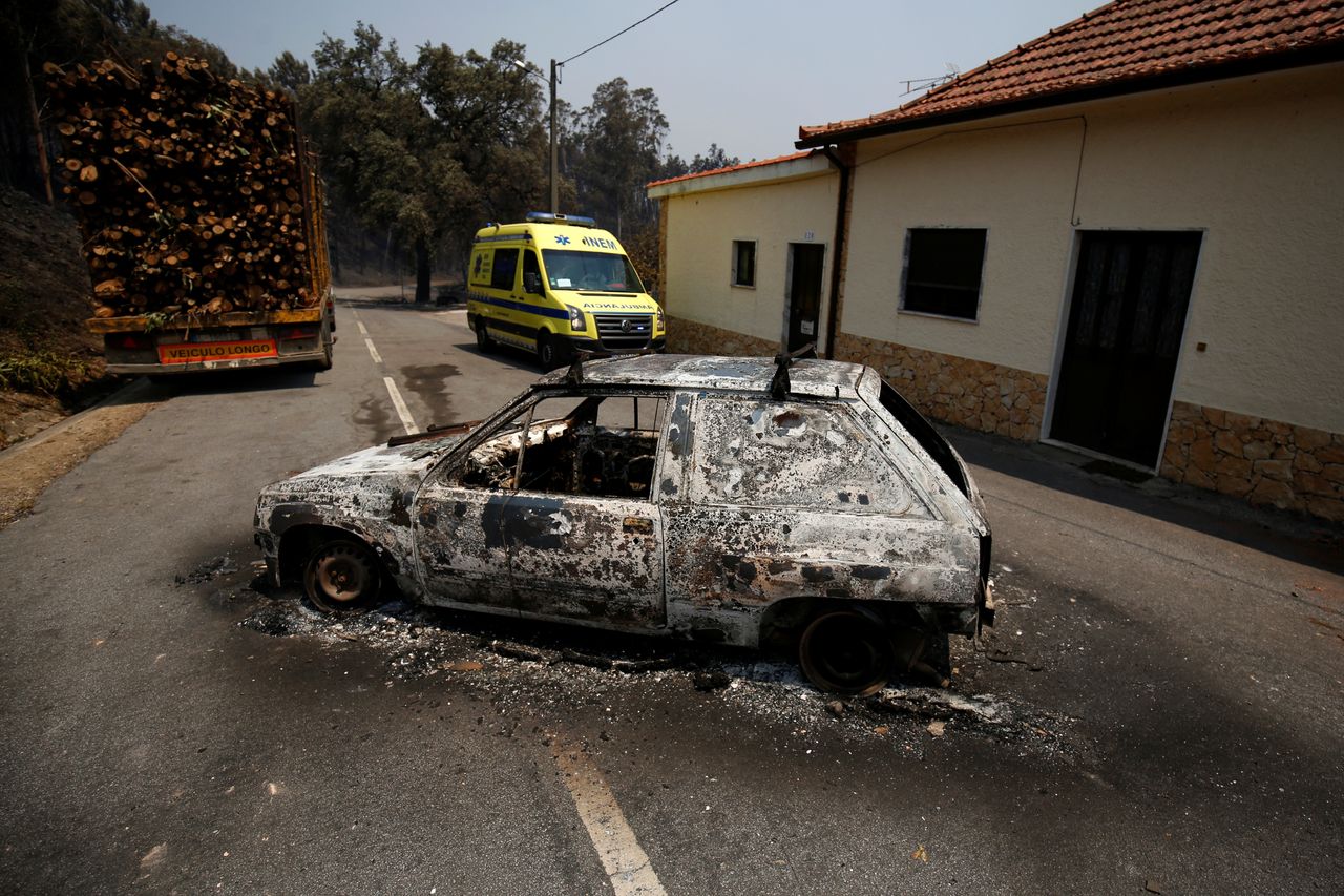 An ambulance drives past a burned car during a forest fire in Figueiro dos Vinhos.