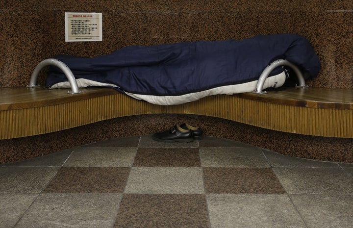 A homeless man snuggles in a sleeping bag on a bench at an underground passage near Sendai Station, December 2013.