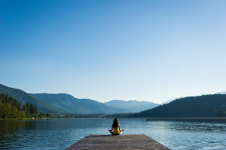 Female meditating doing sukhasana or Easy Pose during a yoga working at a pristine mountain lake stockstudioX via Getty Images