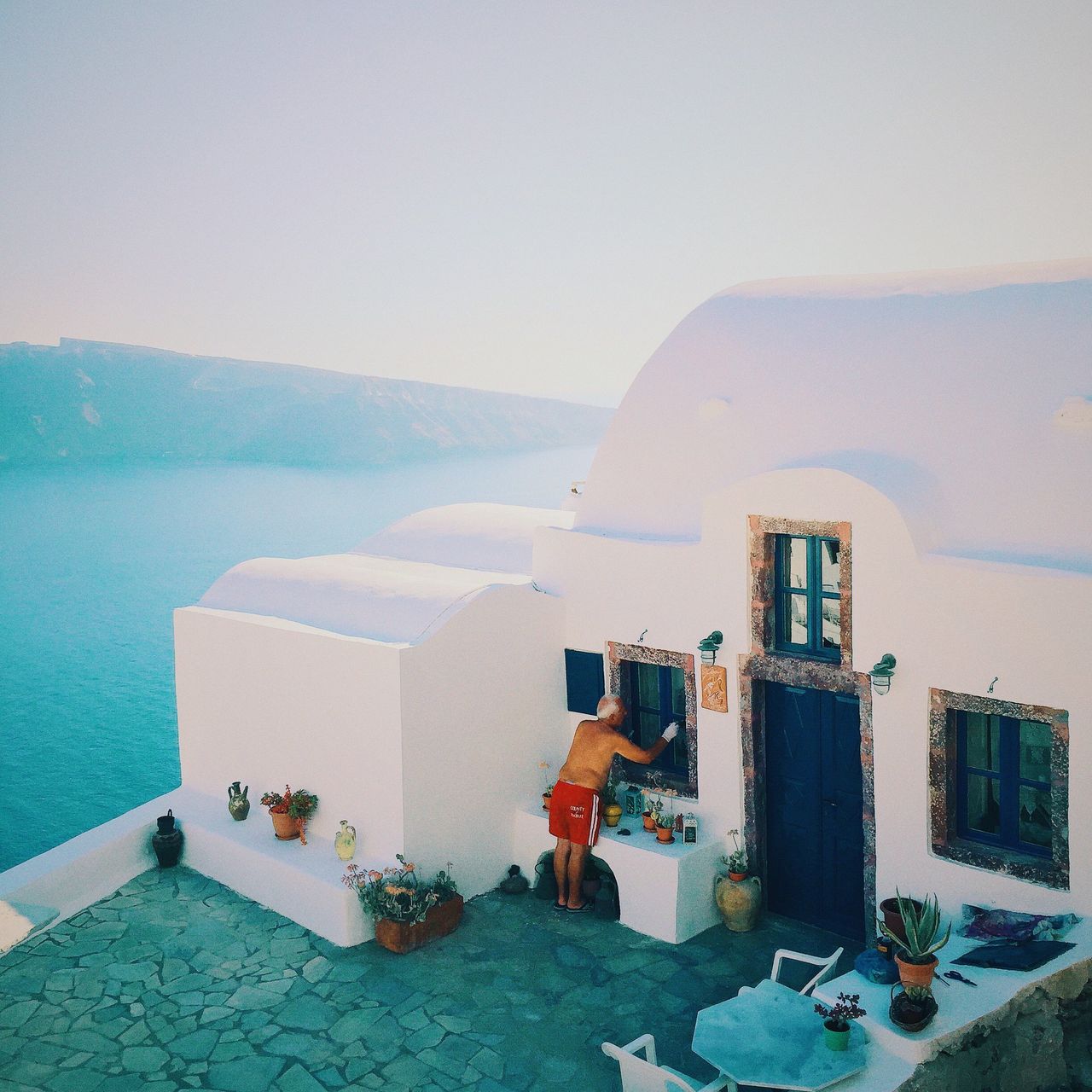 YuMing Guan. Guangdong, China. <strong>2nd Place – Lifestyle.<br><br><em><br></em></strong><em>“This picture was taken in the summer of 2015, in Oia, a beautiful small town of Santorini. Tourists from around the globe gathered at the cliff to see the breathtaking sunset that is known as one of the Greatest Views in the World. Everyone was amazed by the stunning moment with awe and applauds, that’s when this local old man caught my attention. He was so concentrated and undisturbed, as if no crowd or view deserves his attention better than his own windowsill. I guess perhaps in his mind, the Greatest View in the World is HOME.”</em><strong><br></strong>