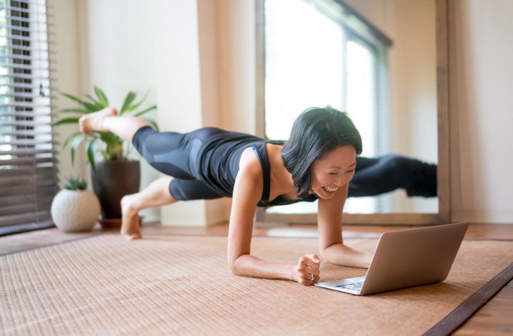 Asian woman exercising at home following a fitness video online andresr via Getty Images