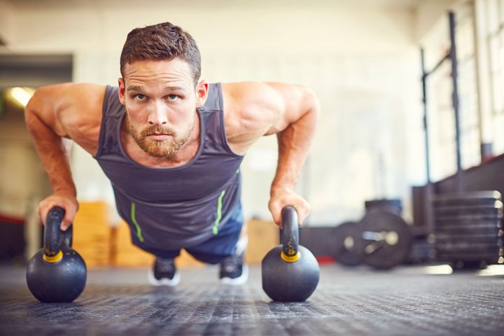 Focused athlete doing push-ups on kettlebells. Male is exercising in gym. He is in health club. Neustockimages via Getty Images
