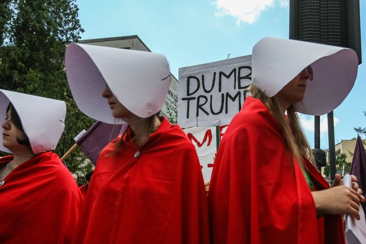 Woman dressed as as characters from The Handmaid's Tale and people holding anti-Trump posters and banners in Warsaw,