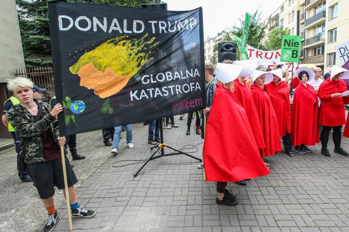 Woman dressed as as characters from The Handmaid's Tale and people holding anti-Trump posters and banners in Warsaw.