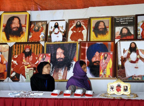 Indian followers of deceased guru Ashutosh Maharaj sit front posters bearing his image at a stall during a congregation at hi
