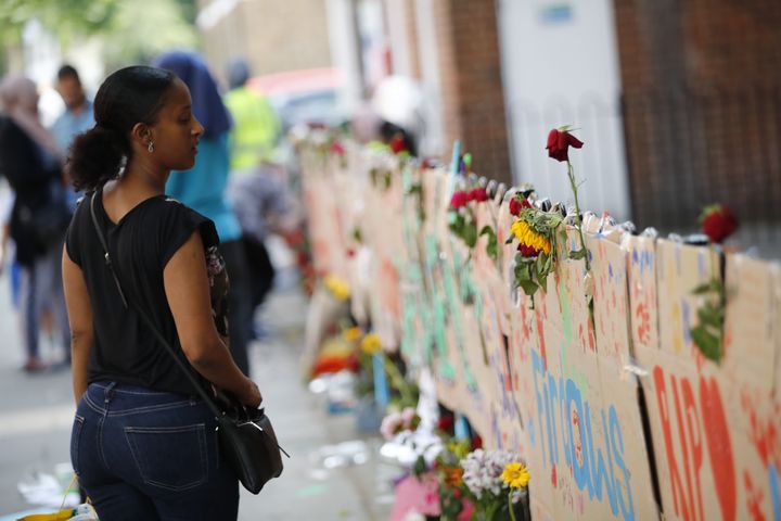 People pause in front of memorial tributes to the victims and the missing from the Grenfell Tower block fire close to the scene in North Kensington, west London, on June 18, 2017