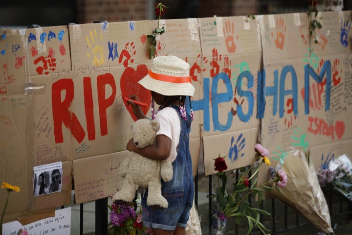 A girl draws on a memorial set against railings in tribute to the victims and the missing from the Grenfell Tower block fire close to the scene in North Kensington, west London.