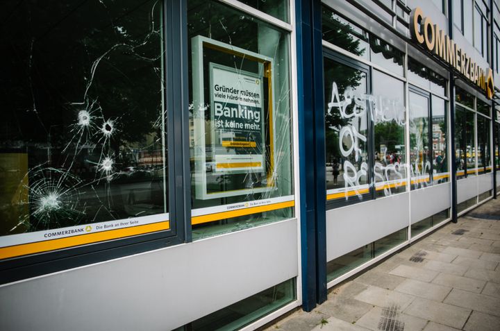 The front of a bank with a smashed window and graffiti 