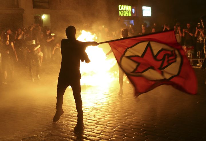 An anti-G20 protestor waves a flag in front of a burning bin 