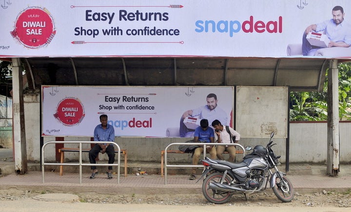 Commuters sit at a bus stop adorned with an advertisement of Indian online marketplace Snapdeal.