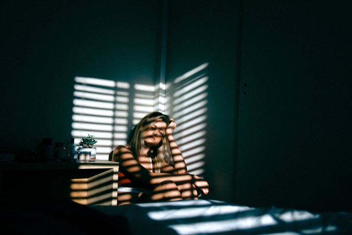 <p>Young woman sitting in the shadows looking sad</p>