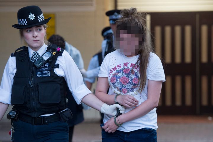 A woman is led away by police after a number of drugs raids in a housing estate in south London