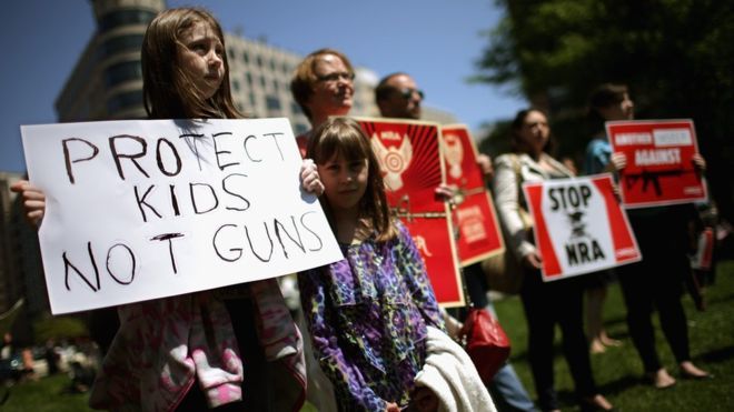 Anti-gun violence demonstrators hold signs condemning the National Rifle Association in Washington, DC