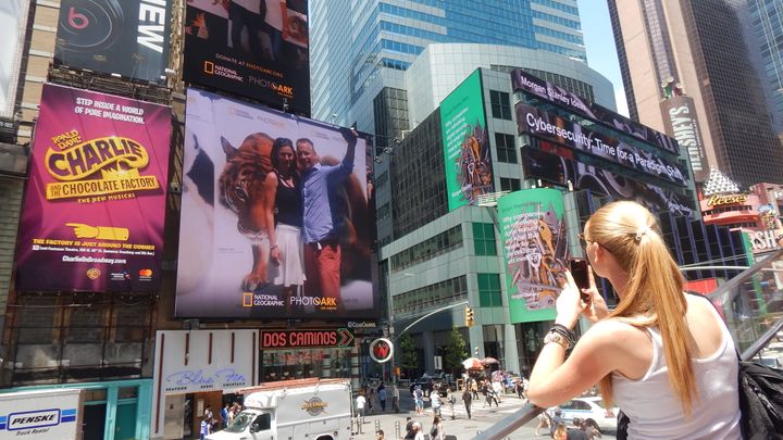Woman in Times Square takes a photo of her #SaveTogether selfie on a digital billboard. 
