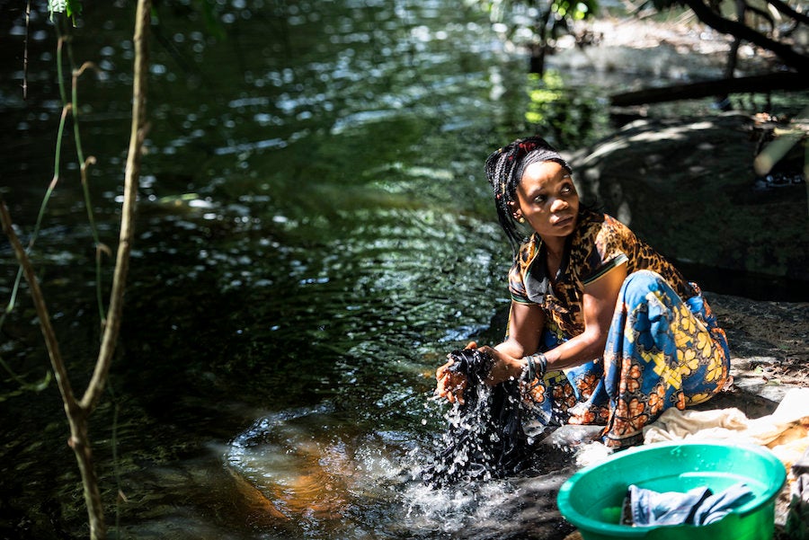 Regine Bora washes clothes by the river while black flies buzz around her.