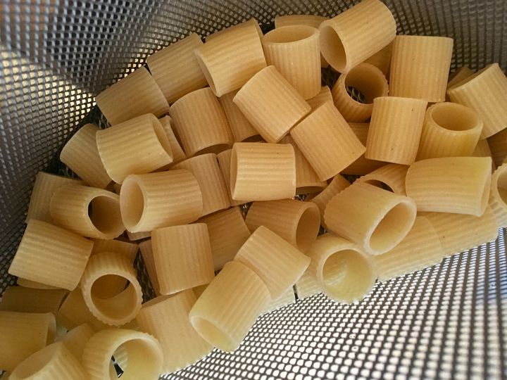 Mezze maniche (half-sleeves) pasta in a basket, ready to submerge in boiling water