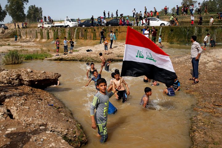 A boy holds the Iraqi flag as he plays in the water with other children during a Friday holiday in the Shallalat district of eastern Mosul. April 21.