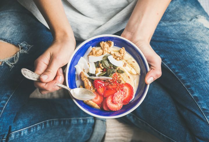 Eating healthy breakfast bowl. Yogurt, granola, seeds, fresh and dry fruits and honey in blue ceramic bowl in woman' s hands. Clean eating, dieting, detox, vegetarian food concept Foxys_forest_manufacture via Getty Images