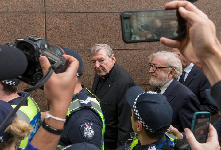 George Pell is surrounded by Australian police and members of the media as he leaves the Melbourne Magistrates Court.