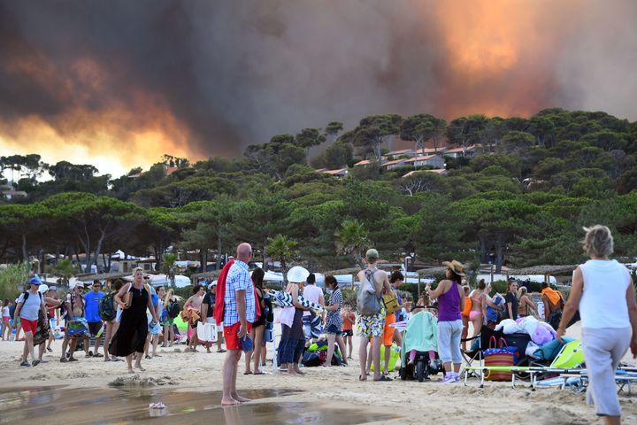 People leave the beach with their belongings as they look at fire burning a forest behind them in Bormes-les-Mimosas, southeastern France, Wednesday.