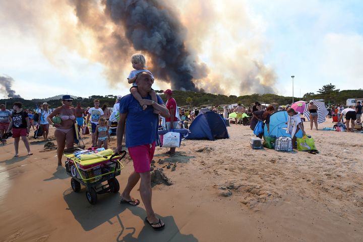 People leave the beach with their belongings as the fire burns a forest behind them in Bormes-les-Mimosas.