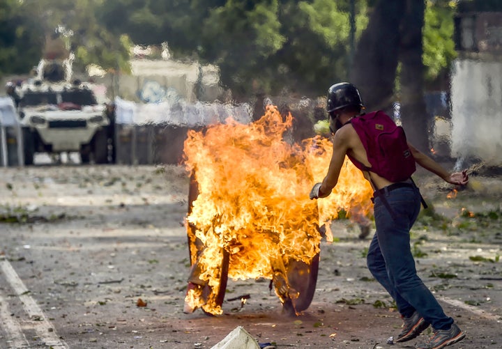 An opposition demonstrator pushes a wooden reel set ablaze toward a line of riot police during clashes in Caracas, Venezuela, on July 26, 2017. 