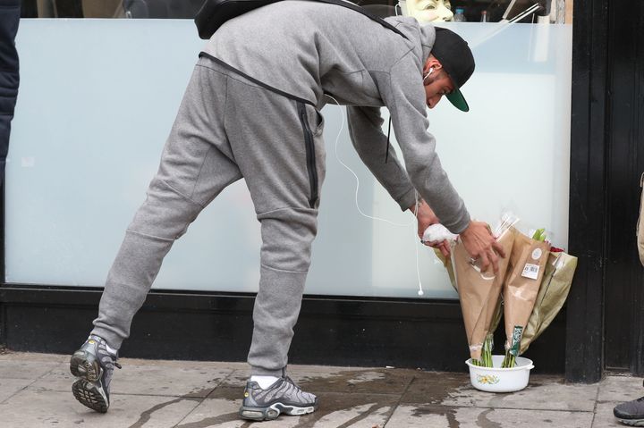 A man lays flowers outside the Kingsland Road shop where Rashan Charles was chased and apprehended, shortly before his death