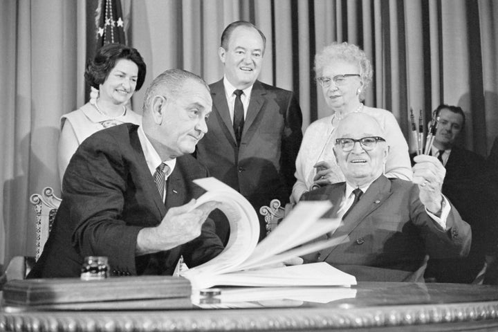 President Lyndon Johnson flips through the pages of the Medicare bill for former President Harry Truman in Independence, Missouri on July 30, 1965. Behind Johnson and Truman are Mrs. Johnson (left), Vice President Hubert Humphrey and Mrs. Truman. 