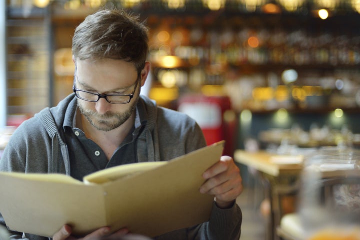 Young man choosing from the menu in the restaurant. Csondy via Getty Images