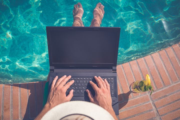High angle view of man sitting at the poolside and using laptop. Travel and technology concepts zoff-photo via Getty Images
