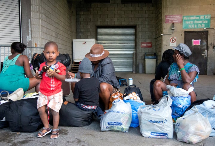 A group of Haitian asylum seekers sit with shopping bags outside the Olympic Stadium, which is being used for temporary housi