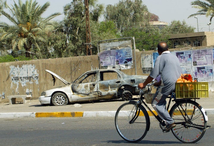 An Iraqi man rides a bicycle passing by a remains of a car in Baghdad, 20 September 2007. The car was burnt during the i