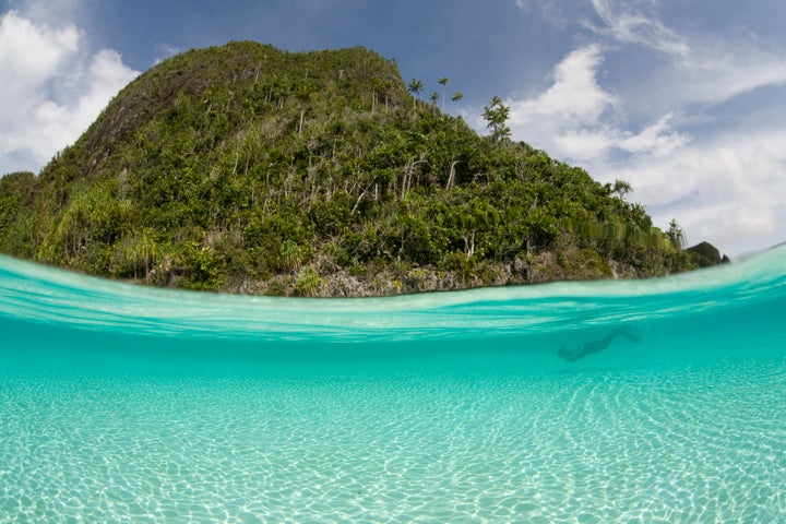 A freediver swims through crystal clear water near a limestone island in Raja Ampat. © Ethan Daniels 