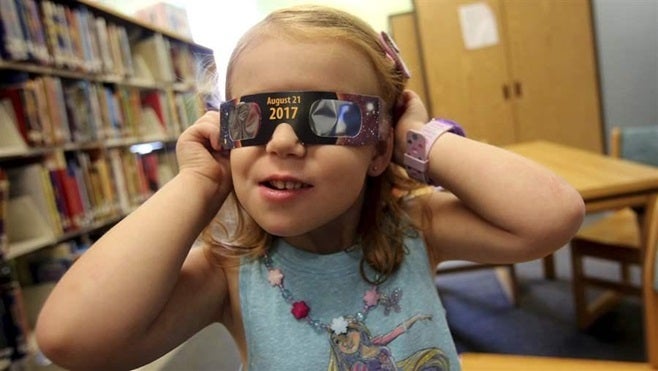 Emmalyn Johnson, 3, tries on her “eclipse glasses” at her local library in North Carolina. Millions of people are expected to