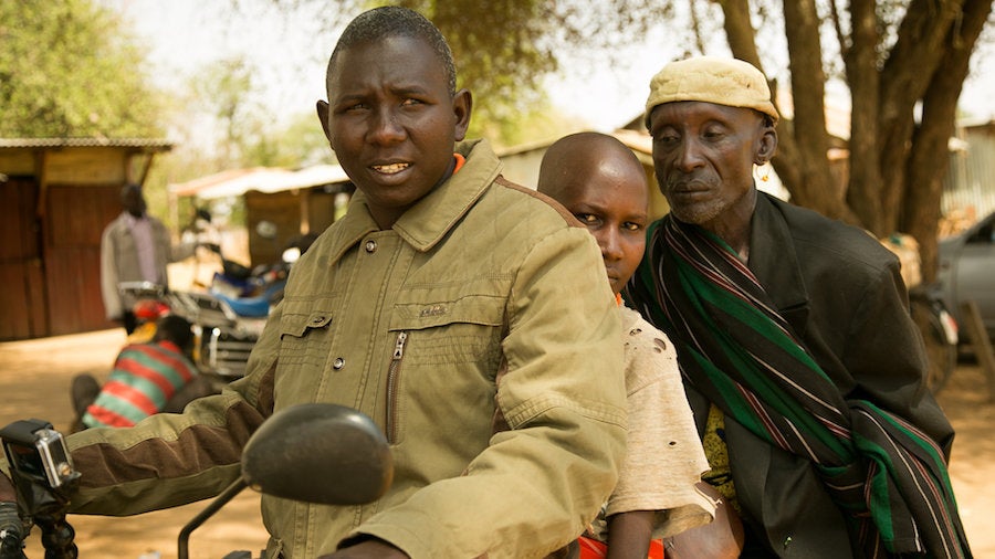 Pkoror Lomerilima, center, sits on a motorbike between his father, right, and community mobilizer Isaac Nyeris, lef