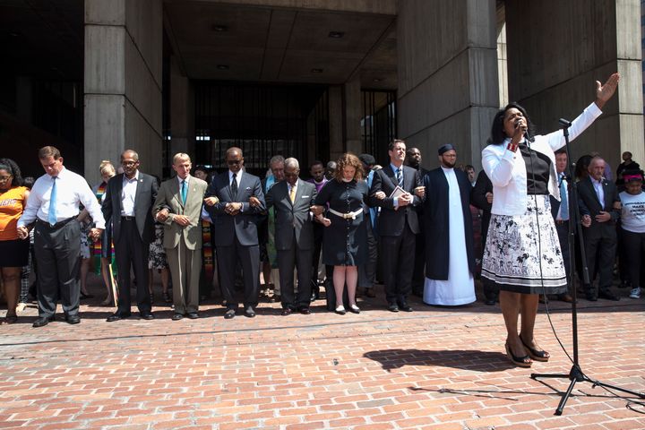 The Rev. Arlene Hall leads a prayer for peace at City Hall Plaza, as Boston Mayor Marty Walsh and Police Commissioner William B. Evans hold hands with clergy ahead of Saturday's rally.