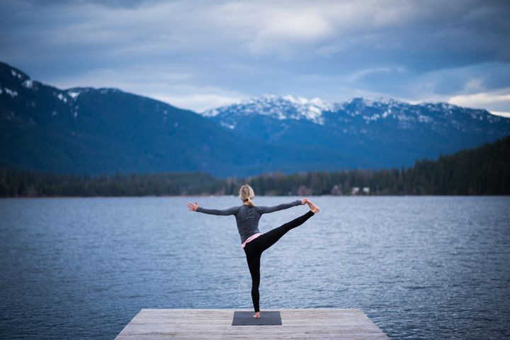 Female doing a tree pose during a yoga working at a pristine mountain lake stockstudioX via Getty Images