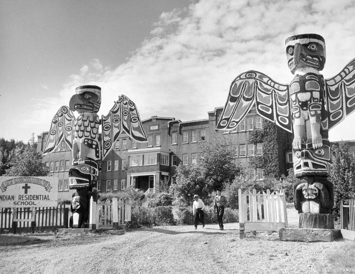 Students walk between two totem poles at St. Michael's Indian Residential School in Alert Bay, British Columbia, in a 1970 photo.