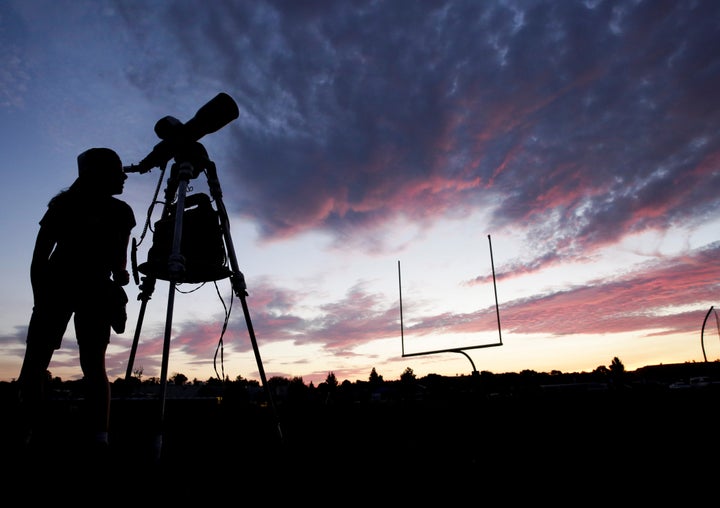 A woman looks through a telescope on the football field at Madras High School the evening before a solar eclipse in Madras, Oregon.