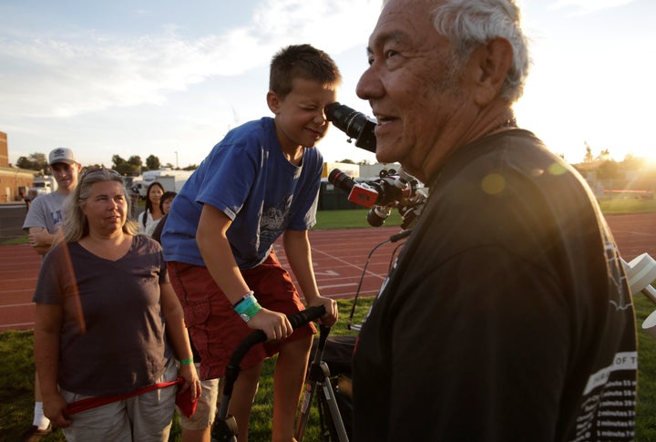 Ken Spencer, right, of Buckeye, Arizona, assists people as they look at the sun through a solar filter-equipped telescope at the Lowell Observatory Solar Eclipse Experience in Madras, Oregon.