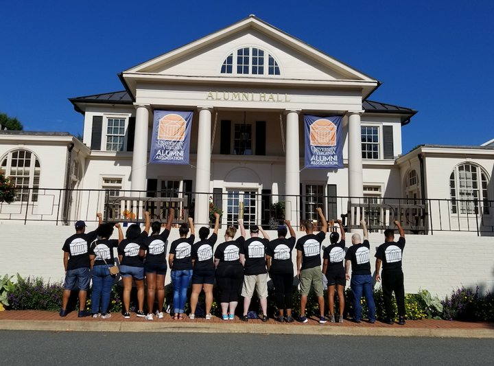 A group of alumni gather on campus and stand in solidarity with their fists raised. 