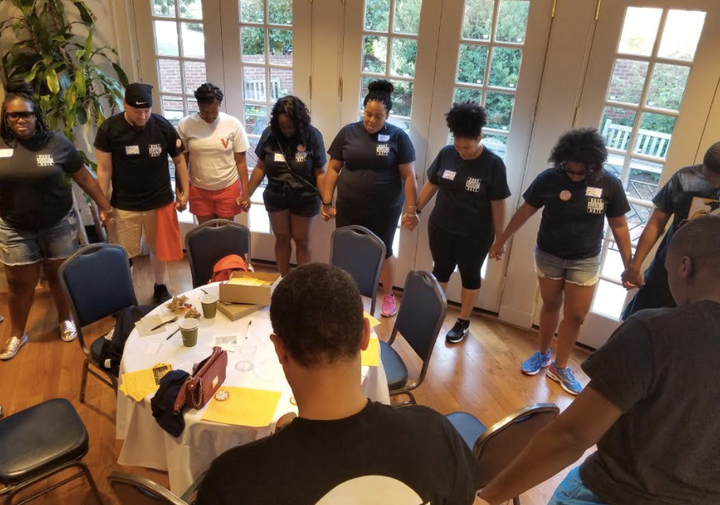 Alumni and students gather around to hold hands as they pray. 