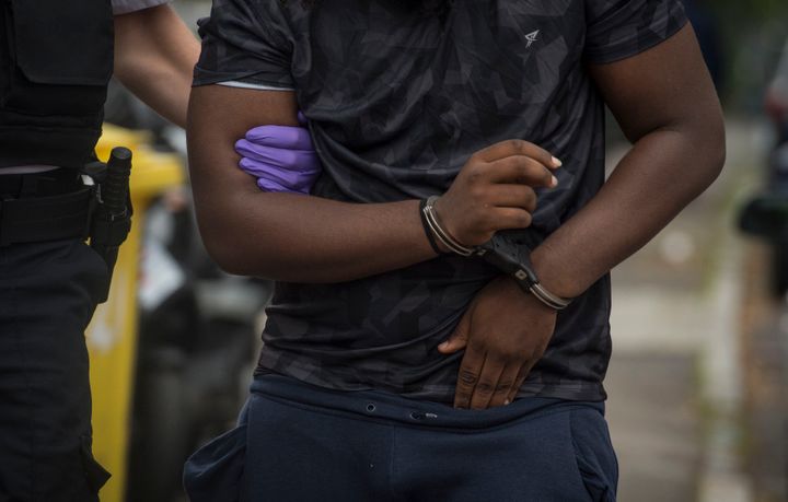 A man is led away by police after being arrested at an address in Lewisham, south east London, following a series of dawn raids across south and west London on Tuesday